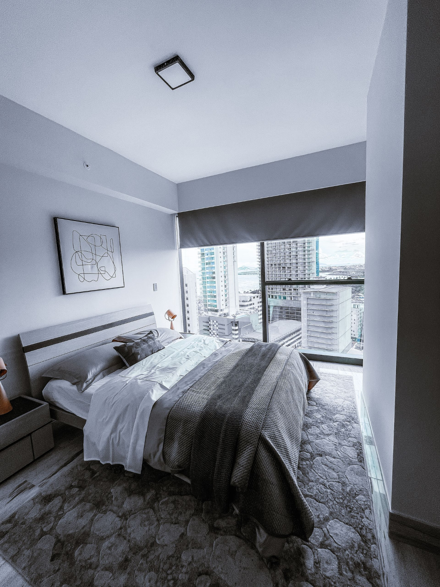 Softly lit modern bedroom in white, grey, and charcoal with a city view